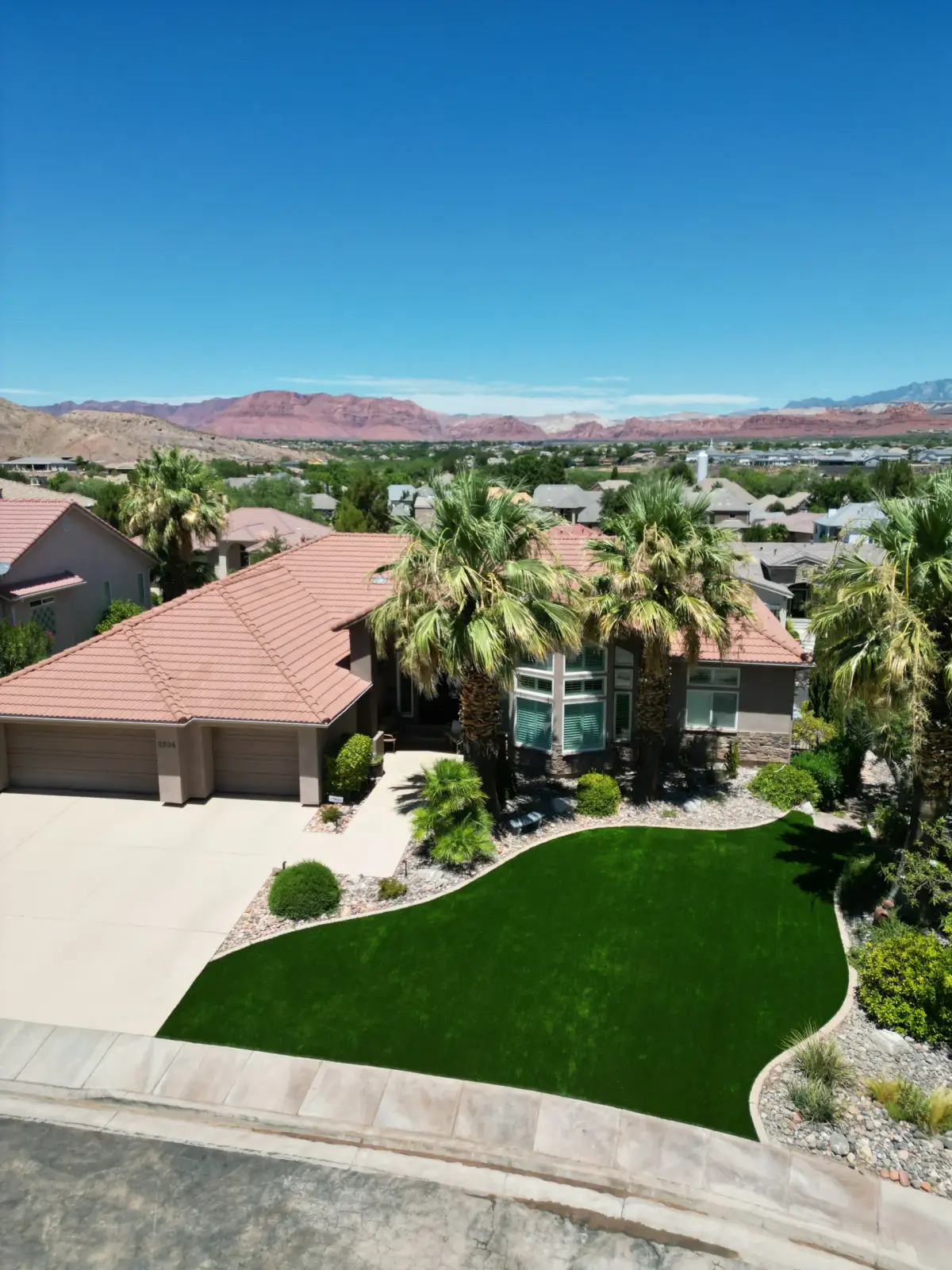 Aerial view of a curved artificial turf lawn beside a St. George home with palm trees
